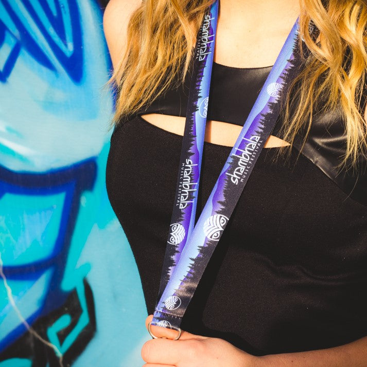 Express yourself with a Shambhala Music Festival lanyard. This blue, purple and black lanyard depicting the forrest surrounding the farm, the Shambhala owl and our 2017 logo is a must-have keepsake item for carrying your keys, ID and more.